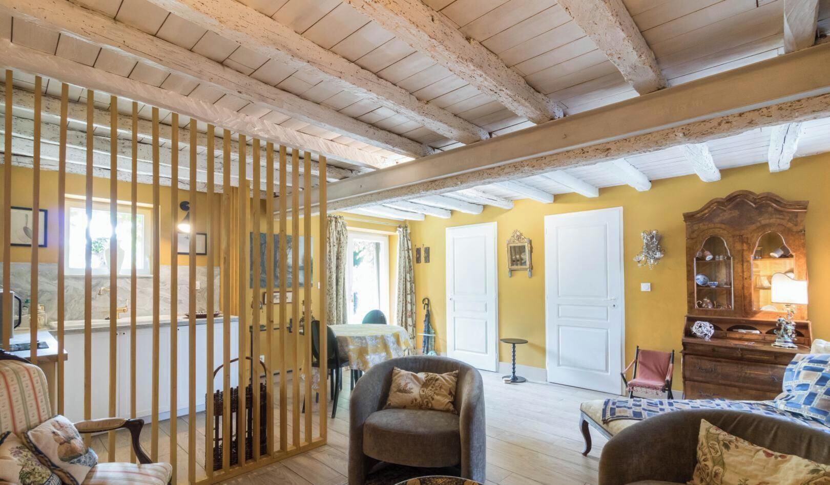 A room with a wooden ceiling, a dining area with a table and chairs, a sofa, and a wooden cabinet with decorative items.