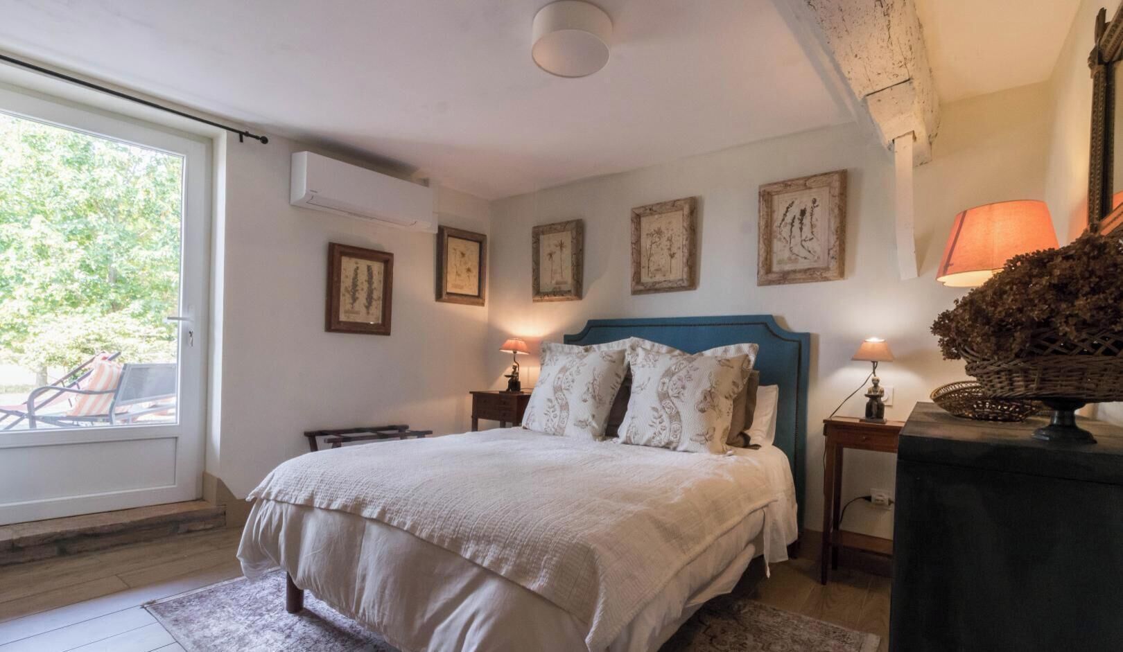 A bedroom with a bed, bedside lamps, a window, and framed pictures on the wall.