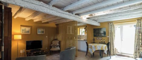 Una habitación con techo de madera, televisor, mesa de comedor con sillas y ventana con cortinas.