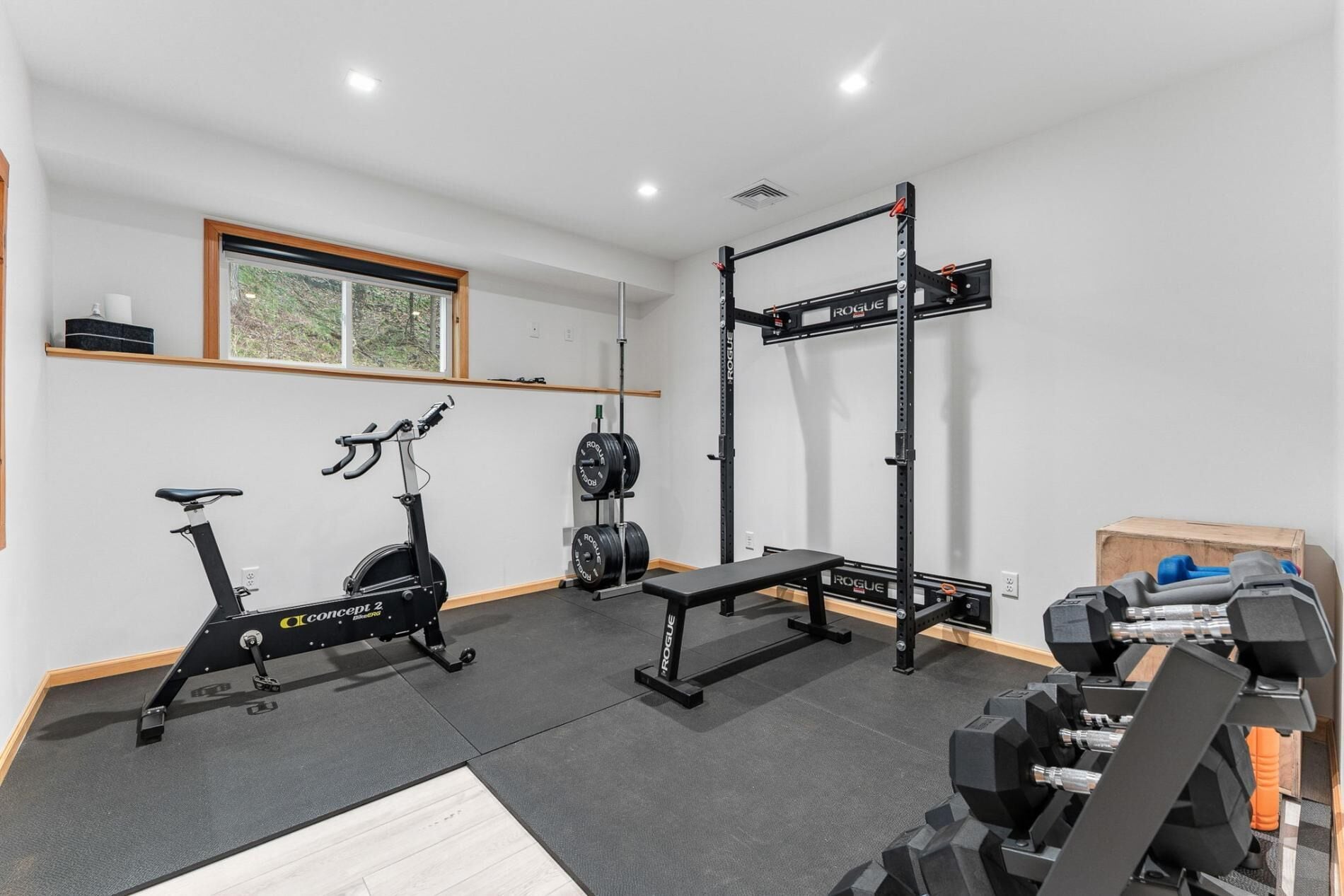 A home gym with a stationary bike, weight bench, squat rack, and dumbbells.