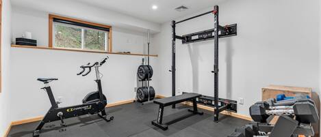 A home gym with a stationary bike, weight bench, squat rack, and dumbbells.