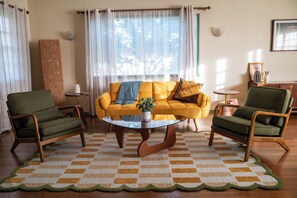A living room with a yellow sofa, two green armchairs, a coffee table, and a patterned rug. - Charming LA Escape w/ Sunroom, Yard & BBQ! (Los Angeles)