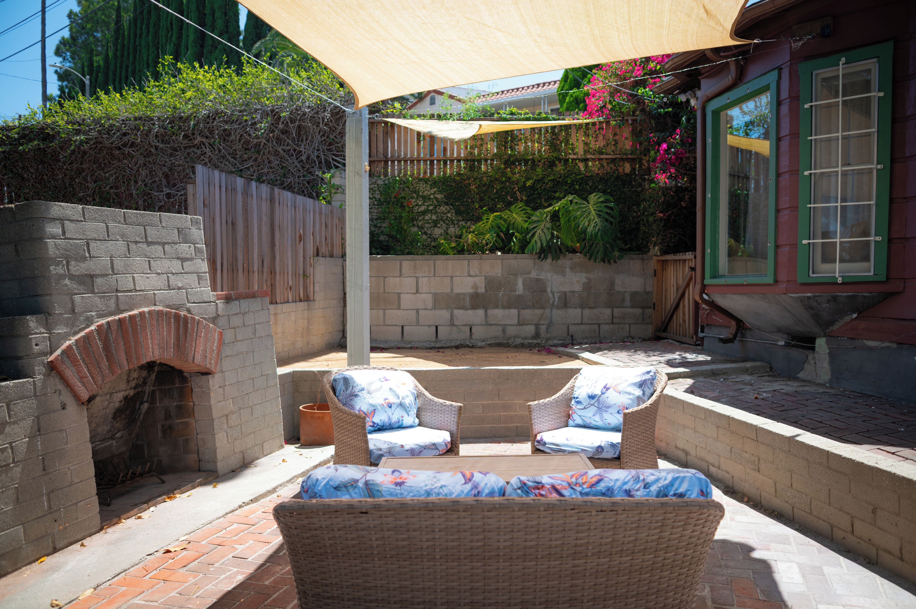 A patio area with two wicker chairs, a brick fireplace, and a wooden fence.