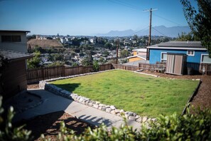 A residential backyard with a grassy lawn, a stone border, and a wooden fence. - Charming LA Escape w/ Sunroom, Yard & BBQ! (Los Angeles)