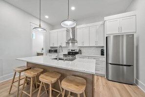 A modern kitchen with white cabinets, stainless steel appliances, and wooden stools. - Sandbar Drift - Where the Coast Slows Down. (Laguna Beach)