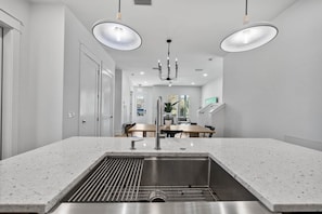 A modern kitchen with a central island, stainless steel sink, and pendant lighting. - Sandbar Drift - Where the Coast Slows Down. (Laguna Beach)
