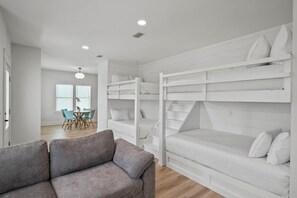 A modern room with bunk beds, a grey sofa, and a dining area with chairs and a table. - Sandbar Drift - Where the Coast Slows Down. (Laguna Beach)