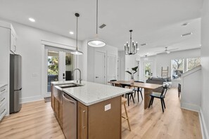 A modern kitchen with a central island, wooden cabinets, and a dining area with a table and chairs. - Sandbar Drift - Where the Coast Slows Down. (Laguna Beach)