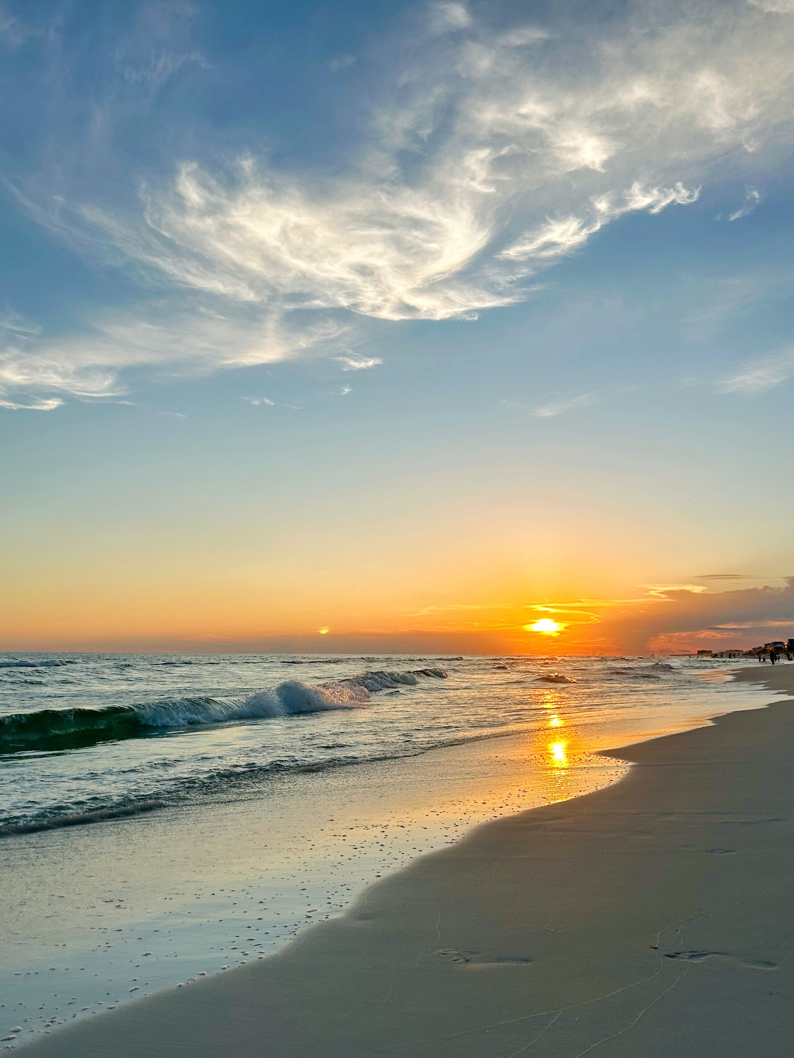 Ein Strand mit Wellen, einem Sonnenuntergang und wolkenlosem Himmel.
