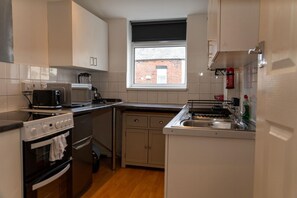 A compact kitchen with a microwave, toaster, and stove. There's a window above the sink, and a fire extinguisher mounted on the wall. - Apartment Sleeps 4 With Wifi & Garden (Bolton)