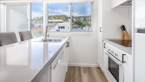 Una cocina moderna con una isla central, muebles blancos y vistas a la ciudad a través de amplios ventanales.