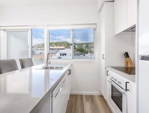 A modern kitchen with a central island, white cabinetry, and a view of the cityscape through large windows. - The Laneway Villas - Central Apartments in the heart of Burleigh Heads - Unit 4 (Gold Coast)