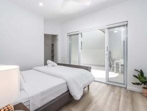 Ein modernes Schlafzimmer mit einem Bett, einem Nachttisch, einer Lampe und einer Glastür, die zu einem Außenbereich führt.
