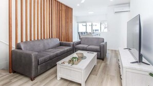 Una sala de estar moderna con dos sofás grises, una mesa de centro blanca, un televisor sobre un mueble bajo y un ventilador de techo.
