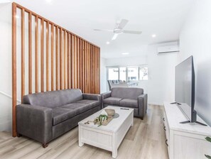 A modern living room with two grey sofas, a white coffee table, a TV on a stand, and a ceiling fan. - The Laneway Villas - Central Apartments in the heart of Burleigh Heads - Unit 4 (Gold Coast)