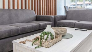 Una sala de estar moderna con dos sofás grises, una mesa de centro blanca con objetos decorativos y un muro de listones de madera.