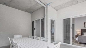 Una mesa de comedor blanca con sillas en una habitación con techo de concreto y un piso de vidrio corredizo que da a una sala de estar.
