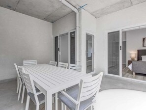 A white dining table with chairs in a room with a concrete ceiling and a sliding glass door leading to a living area. - The Laneway Villas - Central Apartments in the heart of Burleigh Heads - Unit 4 (Gold Coast)