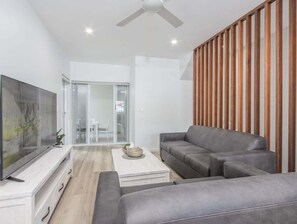Ein modernes Wohnzimmer mit Flachbildfernseher, grauen Sofas, einem Couchtisch und einer raumteilenenden Holzhockerwand.
