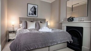 Una camera da letto con un letto grande, un camino, un comodino con una lampada e un quadro appeso al muro.