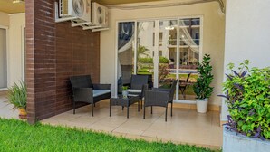Un patio al aire libre con pared de ladrillo, dos sillas de mimbre, una mesita y una planta en maceta.