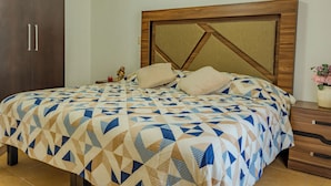 Una cama con colcha de diseño geométrico, cabecera de madera con motivos geométricos y mesita de noche con un florero.