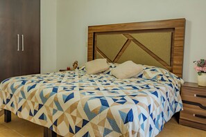 A bed with a geometric patterned bedspread, a wooden headboard with a geometric design, and a nightstand with a vase of flowers. - Acapulco Getaway Pool & Jacuzzi 2 BR (Acapulco de Juárez)