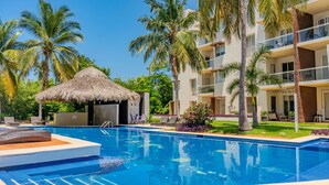 A swimming pool with lounge chairs, a thatched hut, and palm trees. - Acapulco Getaway Pool & Jacuzzi 2 BR (Acapulco de Juárez)