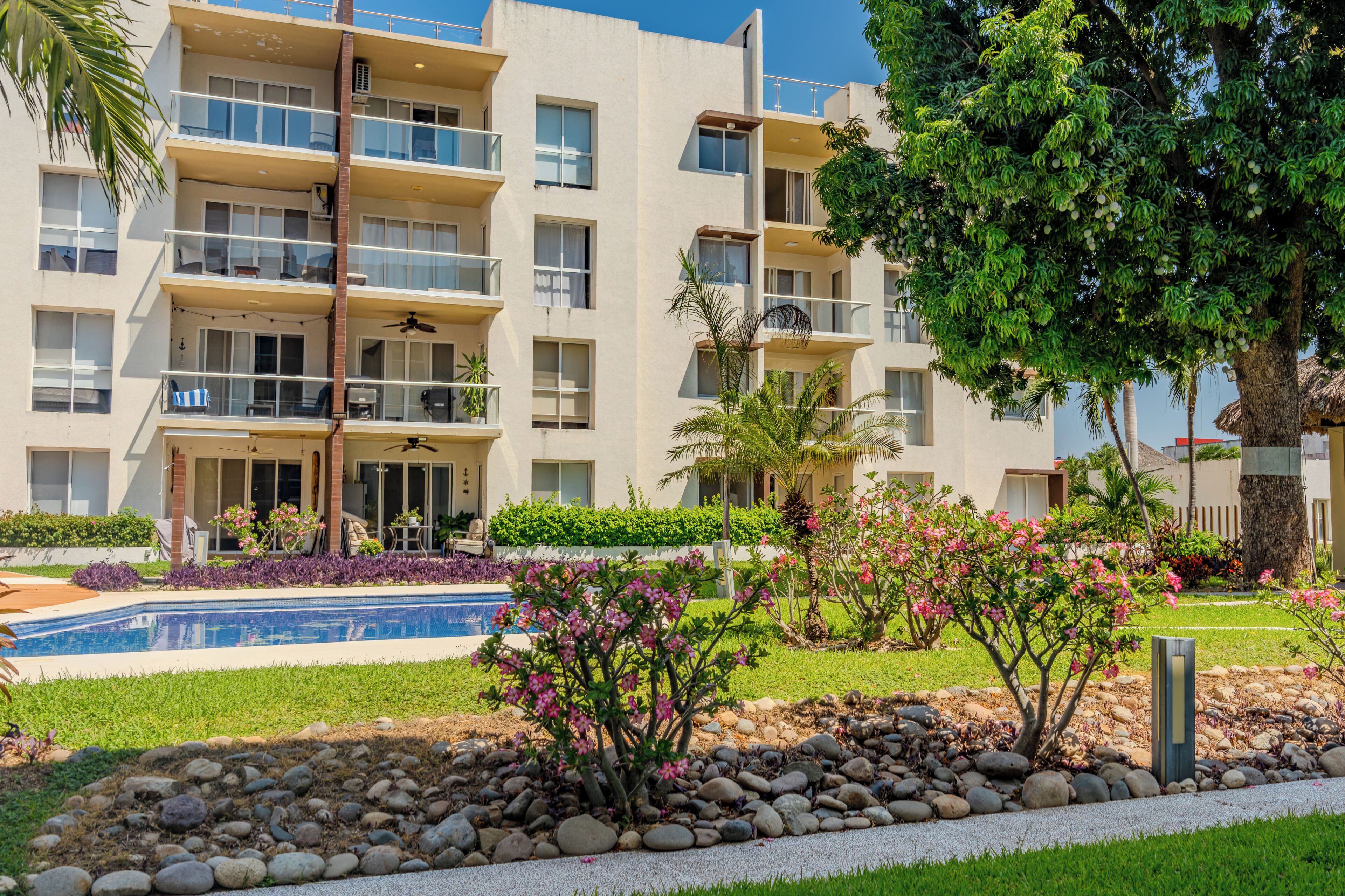 Un edificio residencial de varios pisos con balcones, piscina y jardines ajardinados.
