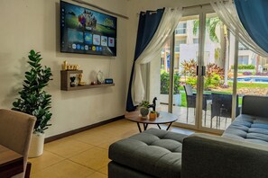 Una sala de estar moderna con una televisión de pantalla plana, un sofá, una mesa de centro y vistas a un jardín a través de un ventanal corredero.