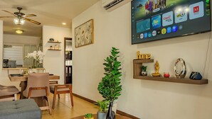 Sala de estar con un televisor de pantalla plana montado en la pared, mostrando varias aplicaciones. Se observa un comedor con mesa y sillas, y una cocina al fondo.