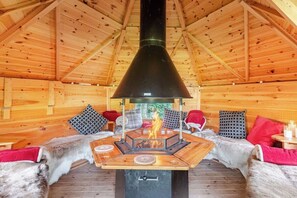 Ein gemütliches Blockhaus-Interieur mit einem zentralen Holzofen, Holzwänden und Sitzgelegenheiten mit Fellbezügen.