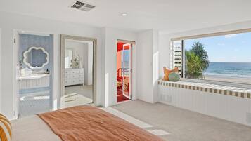 A bedroom with a large bed, a bathroom with a mirror, and a view of the beach.