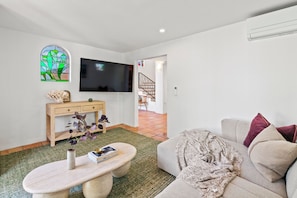 A living room with a flat-screen TV, a wooden console table, a sofa, and a staircase leading to another level. - The Beachhouse by Sandbox - Entire Luxury Beachfront Home with Sauna and Steam Shower in Palm Beach (Palm Beach)