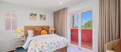 Camera d'albergo con un letto, un comodino, una lampada, una finestra con tende e vista all'esterno.