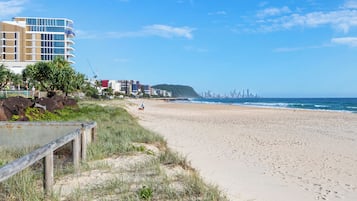 Ein Strand mit einer Holzlattenverkleidung, einer Rasenfläche und einer Stadtkulisse im Hintergrund.