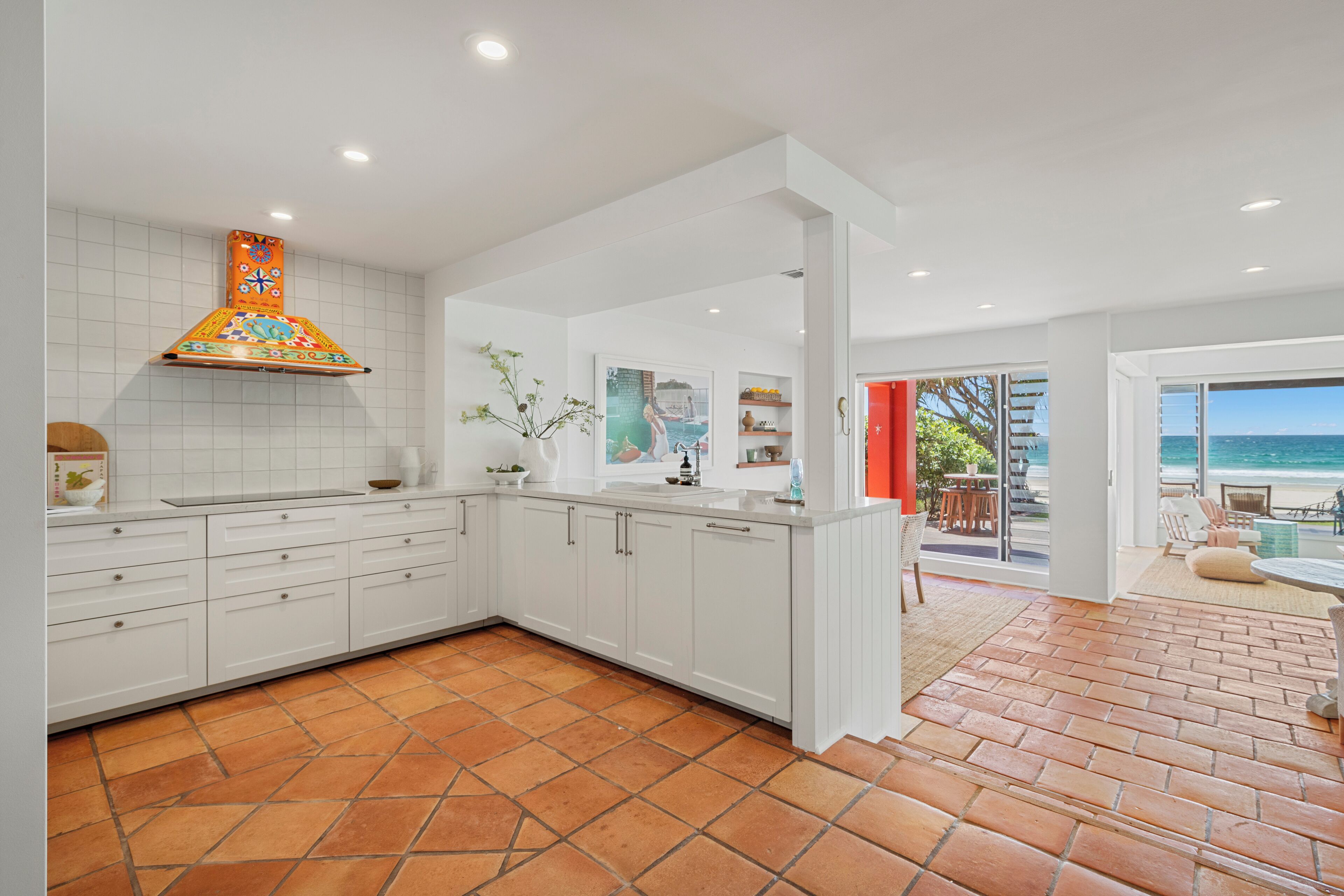 A modern kitchen with white cabinets, a colorful backsplash, and a view to a patio with outdoor seating.