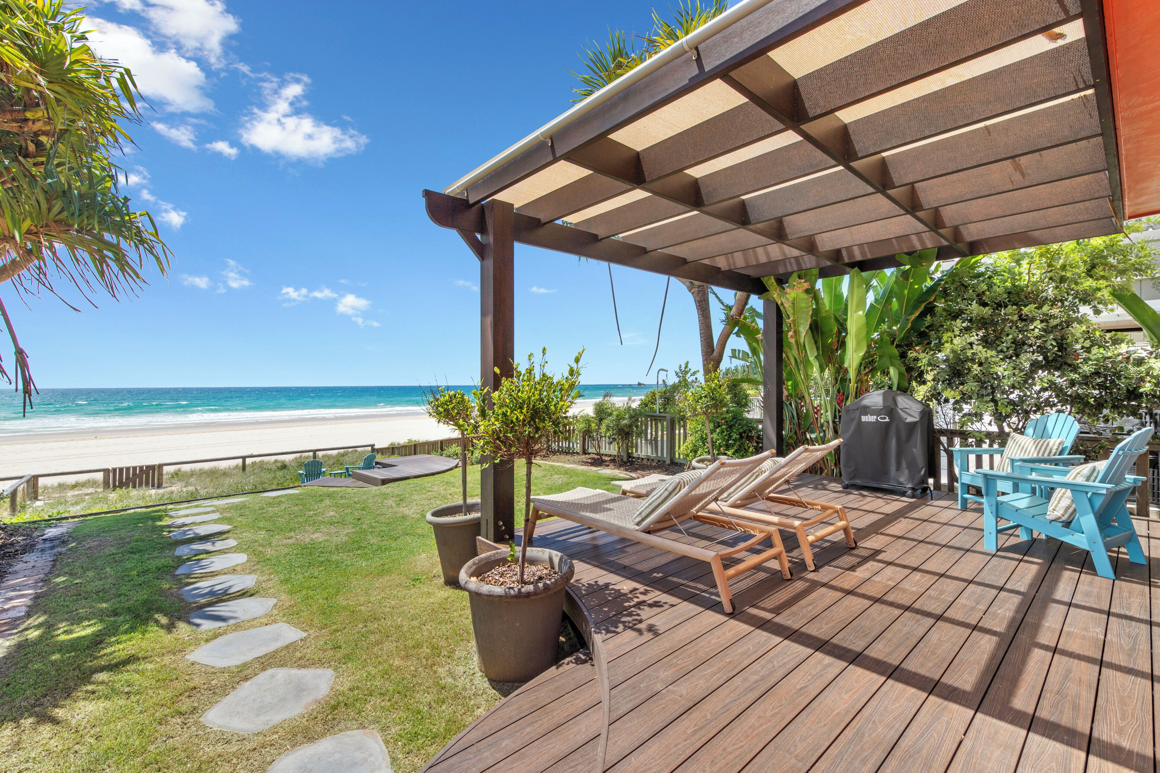 A wooden deck with lounge chairs and a grill, overlooking a beach.