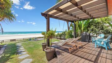 A wooden deck with lounge chairs and a grill, overlooking a beach.
