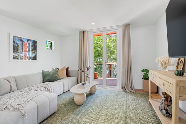 A modern living room with a sofa, coffee table, and a view through a glass door to an outdoor area. - The Beachhouse by Sandbox - Entire Luxury Beachfront Home with Sauna and Steam Shower in Palm Beach (Palm Beach)