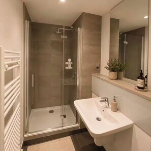Ein modernes Badezimmer mit einer gläsernen Duschkabine, einem weißen Waschbecken und einem Spiegel darüber.