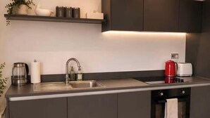 A modern kitchen with a built-in sink, a coffee maker, and a toaster. - Salford Serenity - Modern 2 Bedroom Apartment (Salford)