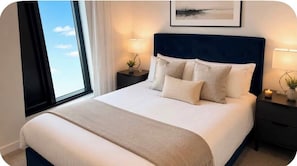 Ein Hotelzimmer mit einem großen Bett, zwei Nachttischen, einem Fenster mit Vorhängen und einem gerahmten Bild an der Wand.