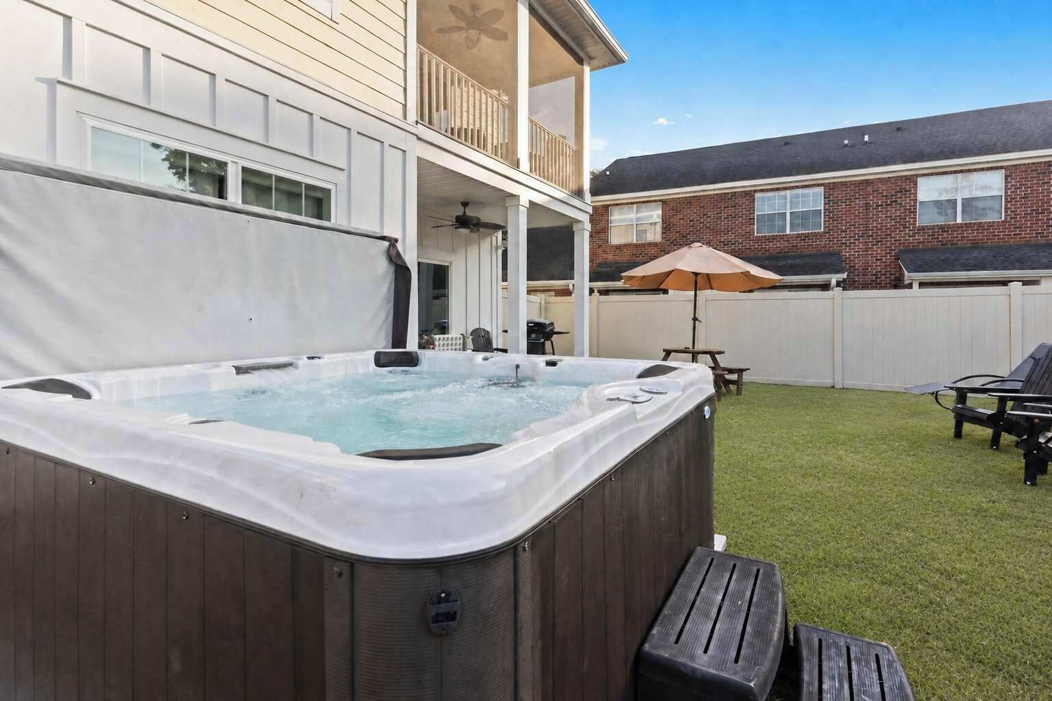Een achtertuin met een jacuzzi, een overdekt terras en een stenen huis op de achtergrond.