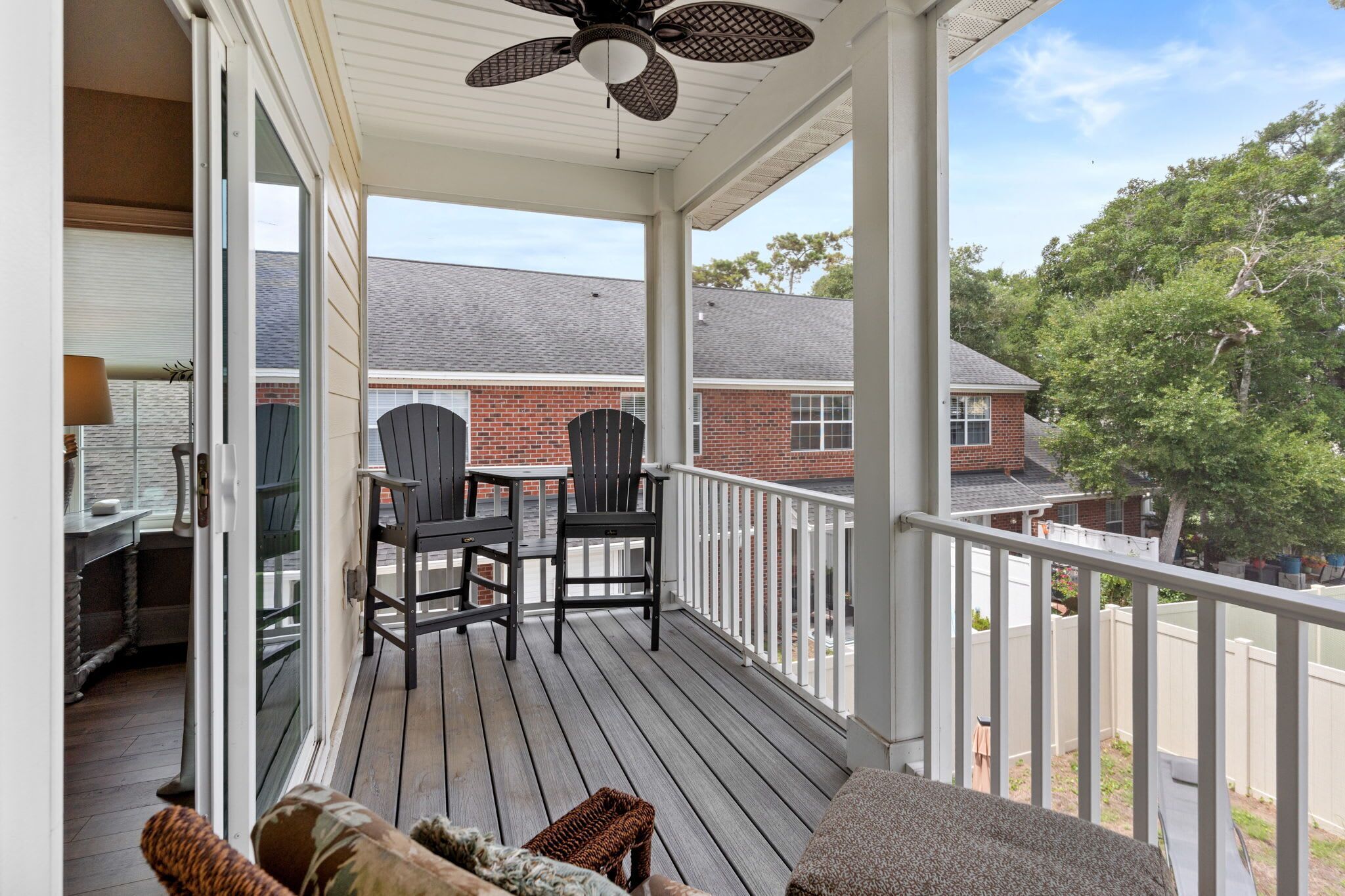 Une véranda couverte avec deux fauteuils Adirondack, une table et un ventilateur de plafond.