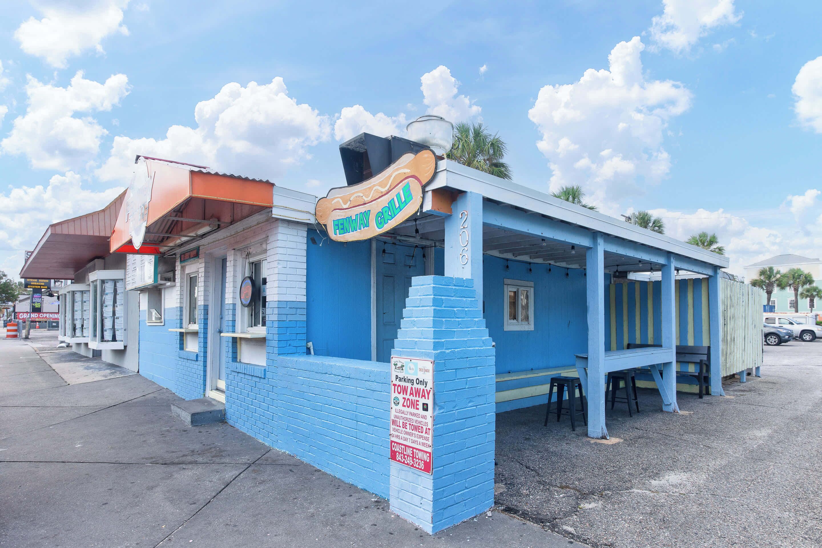 A blue building with a sign reading 'FENWAY GRILL' and a 'TOW AWAY ZONE' sign.