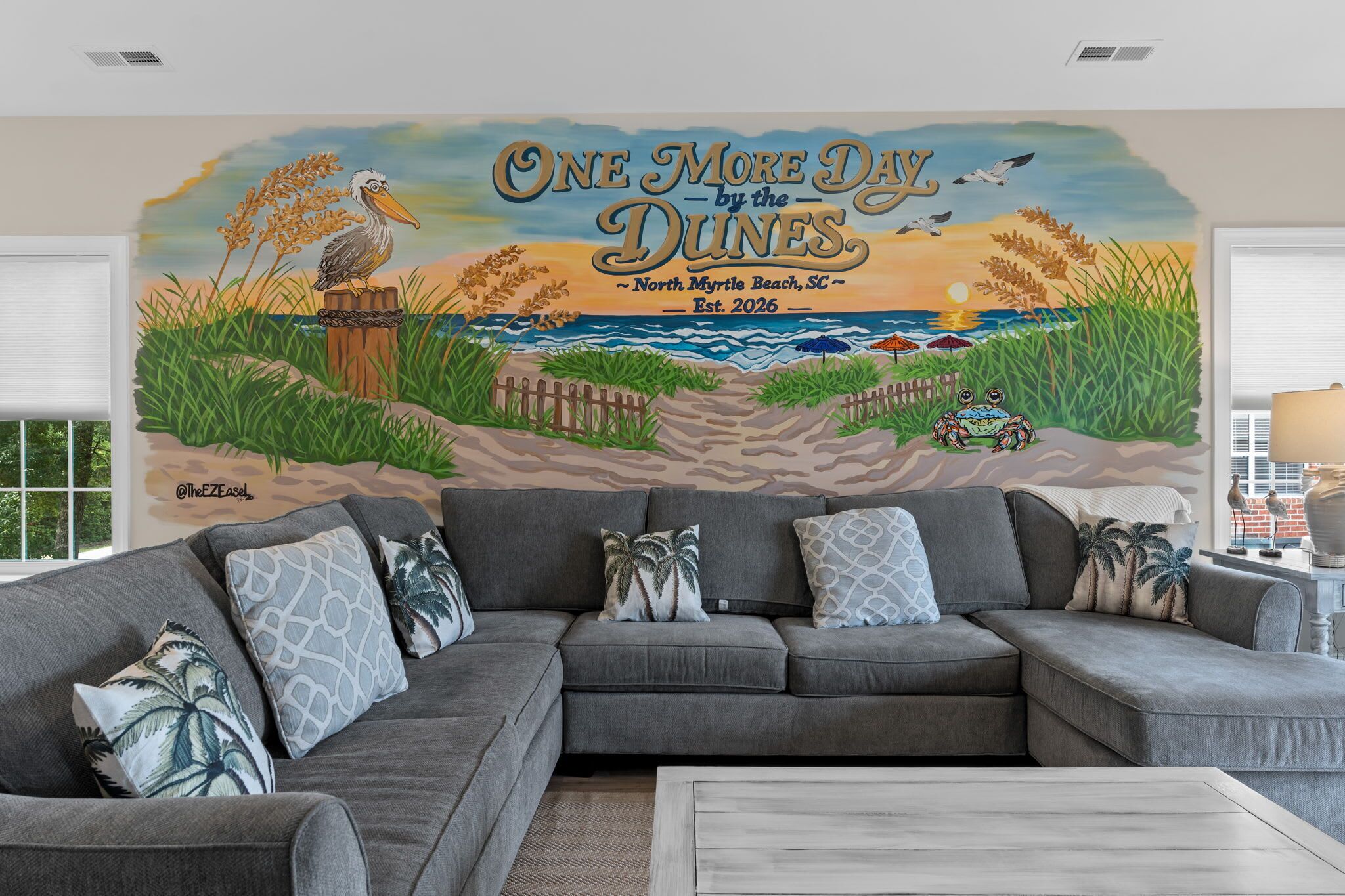 A living room with a large mural of a beach scene, a grey sectional sofa, and decorative pillows.