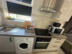 A compact kitchen with a washing machine, an oven, a microwave, and a sink.