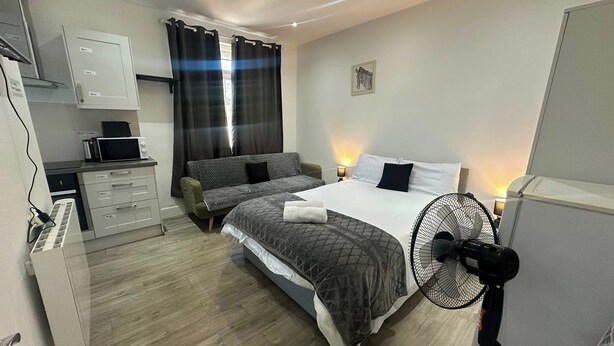 A bedroom with a bed, bedside table, lamp, and a standing fan.