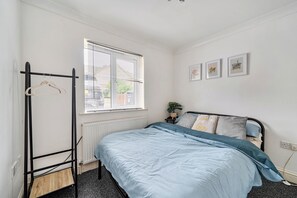 A bedroom with a bed, a radiator, a window with blinds, a coat rack, and a wall with framed pictures. - 3 Bed - Sleeps 6 - Parking - Central Canterbury (Canterbury)